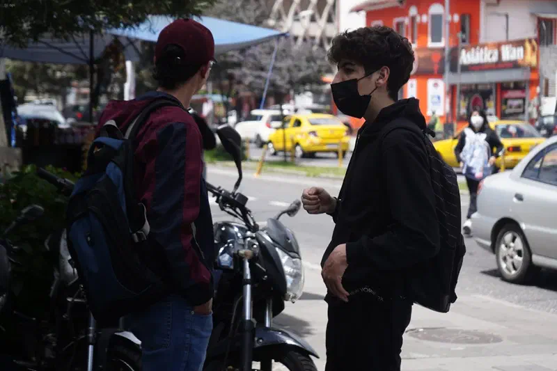 Dos jóvenes conversan en una calle comercial.
